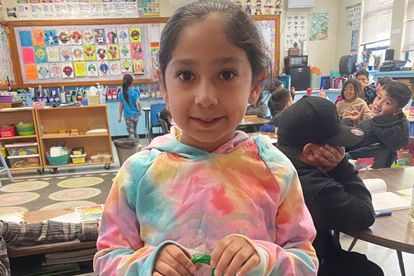 A little girl in a tie-dyed hoodie smiles holding a prize bag