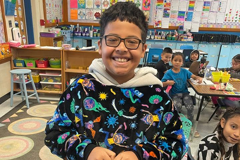 A boy in glasses and a space-themed hoodie smiles holding a prize bag